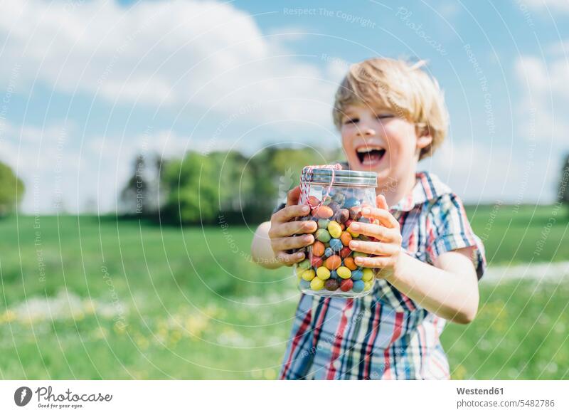 Glücklicher Junge im Freien, der ein Glas mit Geleebohnen hält halten Buben Knabe Jungen Knaben männlich Geleebonbon Spaß Spass Späße spassig Spässe spaßig Kind