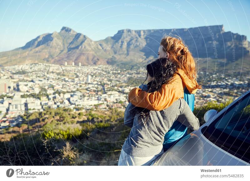 Südafrika, Kapstadt, Signal Hill, zwei junge Frauen, die sich gegen ein Auto lehnen, das die Stadt überragt stehen stehend steht weiblich umarmen Umarmung