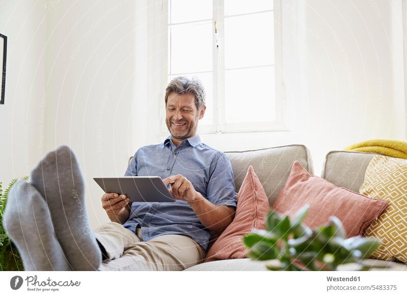 Mann sitzt zu Hause auf dem Sofa und benutzt ein digitales Tablett Online sitzen sitzend Entspannung entspannt Entspannen relaxen entspannen Männer männlich