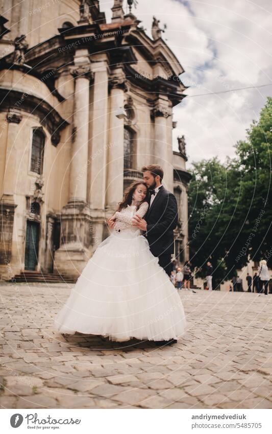 Stilvolle Braut und Bräutigam sanft umarmt auf europäischen Stadtstraße. Gorgeous Hochzeit Paar von Jungvermählten umarmt in der Nähe von alten Gebäude. romantisch sinnlichen Moment der Jungvermählten