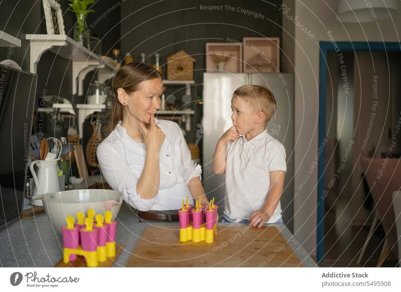 Frau und Junge lecken Finger und machen Eis am Stiel in der Küche Mutter Sohn lutschen Blick Speiseeis gegossen niedlich Familie Herstellung Liebe Dessert