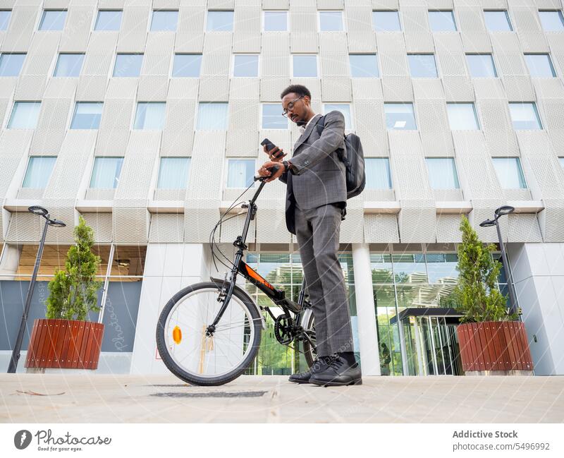 Schwarzer Geschäftsmann mit Smartphone und Fahrrad Mann Talkrunde Fokus formal Großstadt Straße Telefonanruf Browsen Anzug männlich Afroamerikaner schwarz Text