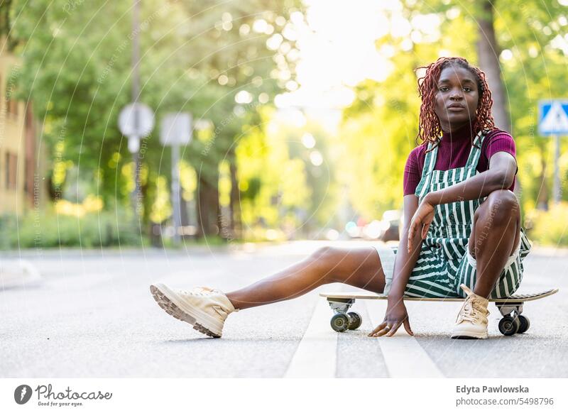 Porträt einer schwarzen nicht-binären Person mit einem Skateboard auf der Straße sitzend echte Menschen positiv selbstbewusst Erwachsener junger Erwachsener