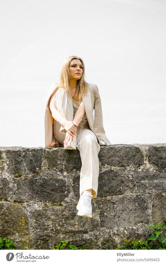 Junge Frau sitzt auf einer Mauer. Lifestyle Freizeit jung blond Pferdeschwanz Freude Portrait Glück Blondine entspannt Erholung hübsch attraktiv glücklich