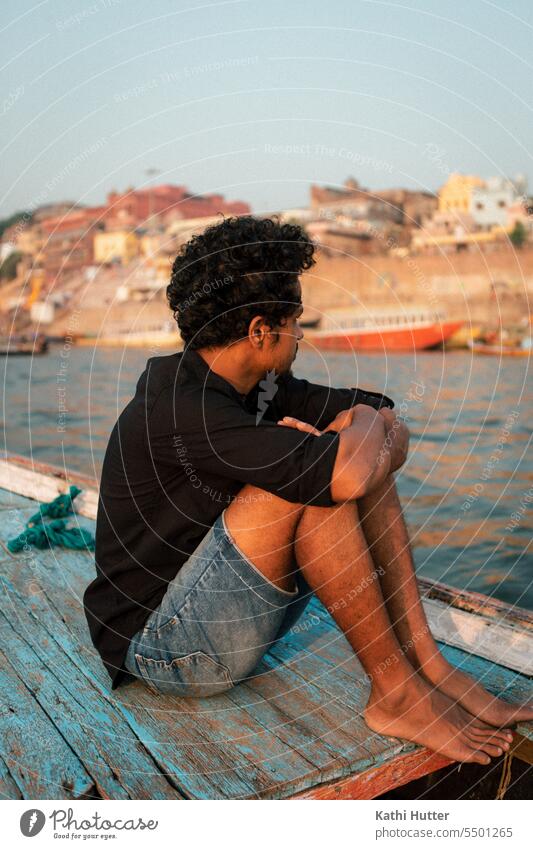 ein junger Mann sitz au einem Holzboot in Varanasi Boot fahren Wasser Wasserfahrzeug Ferien & Urlaub & Reisen Schifffahrt Farbfoto Außenaufnahme Tourismus