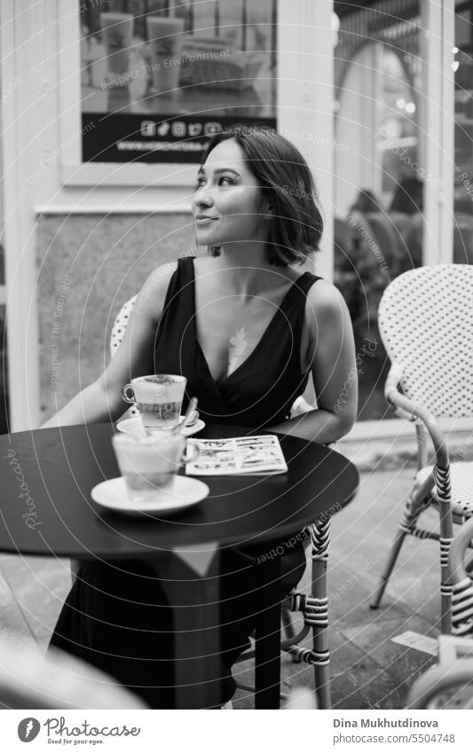 schöne Frau in schwarzem Kleid im Café oder Restaurant Terrasse trinken Kaffee. Elegantes weibliches Porträt. Mode und Stil Konzept. schwarz auf weiß Monochrom