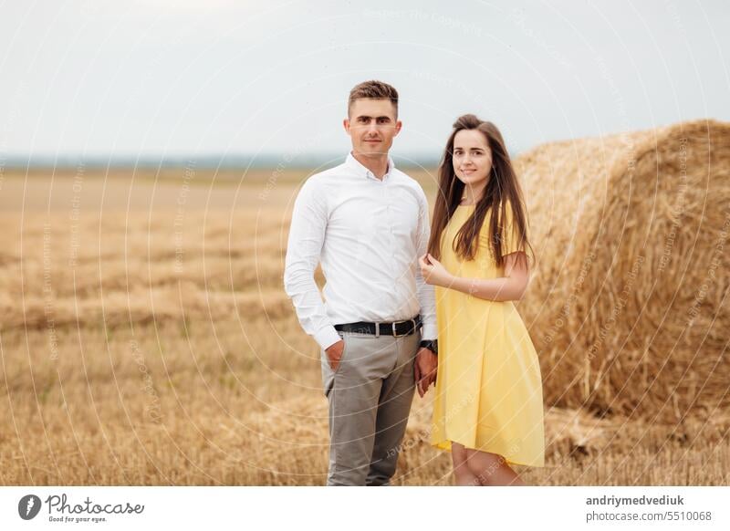 Foto von freudigen Paar Mann und Frau zu Fuß durch goldene Feld mit Haufen von Heuhaufen und umarmt zusammen während sonnigen Tag Liebe jung Porträt Landschaft