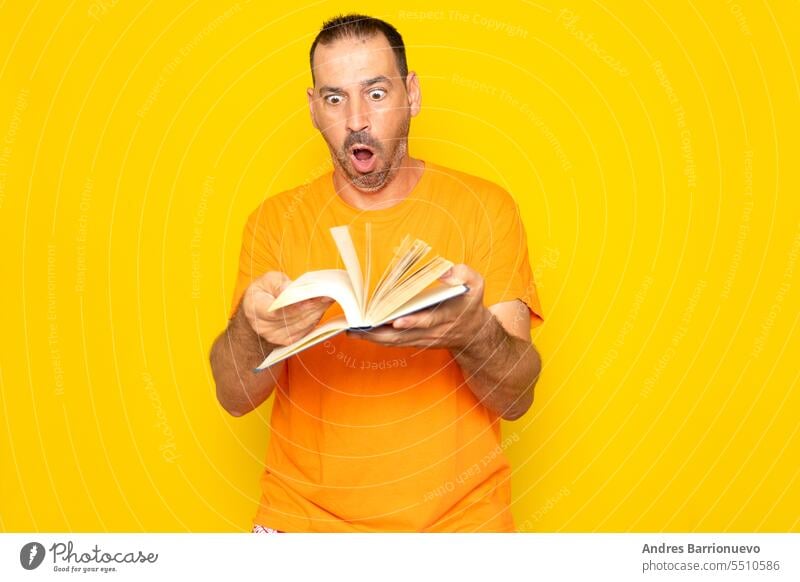 Bärtiger hispanischer Mann in den 40ern blättert sichtlich erregt in einem Buch, isoliert auf gelbem Studiohintergrund. Bildung lernen Notebook klug überrascht