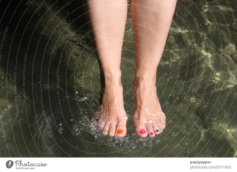 Mit bunten Fußnägeln – Frau nimmt kaltes Fußbad am See Bunte Fußnägel Füße hoch Beine Barfuß Zehen Bunte Zehen Zehennagel Zehenspitze Zehenspitzen Zehennägel