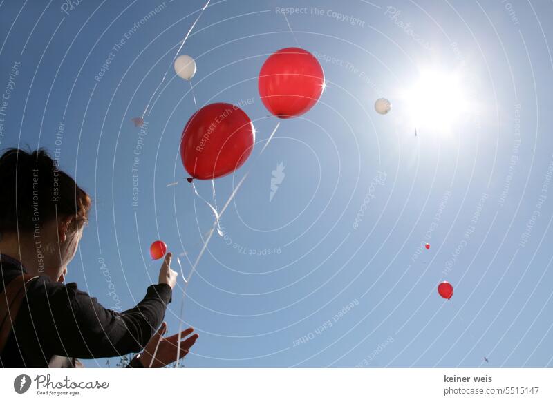 Nicht erkennbare Personen lassen rote und weiße Luftballons in den Himmel fliegen der Sonne entgegen blau Menschen Ballons Sonnenstrahlen anonym Licht