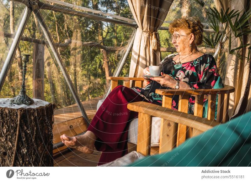 Ältere Frau ruht sich in Glamping-Kuppel aus Freizeit glamourös Heißgetränk Urlaub Rentnerin Senior räkeln Armsessel älter ruhen Tee trinken Landschaft Tasse