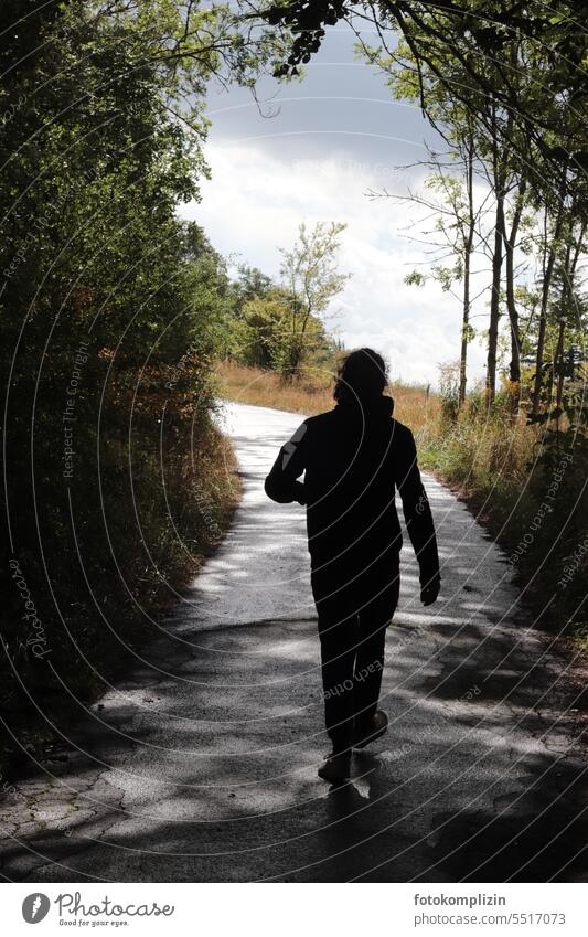 Person läuft von einem dunklen Fußweg in die Helligkeit Mensch Natur spazieren laufen wandern gehen unabhängig selbstständig frei alleine aktiv Wanderer