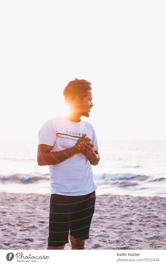 Eine junger Mann am Meer mit Wind in den Haaren und dem Sonnenuntergang. Sonnenlicht Außenaufnahme Mensch Erwachsene Farbfoto Junger Mann Gegenlicht Natur