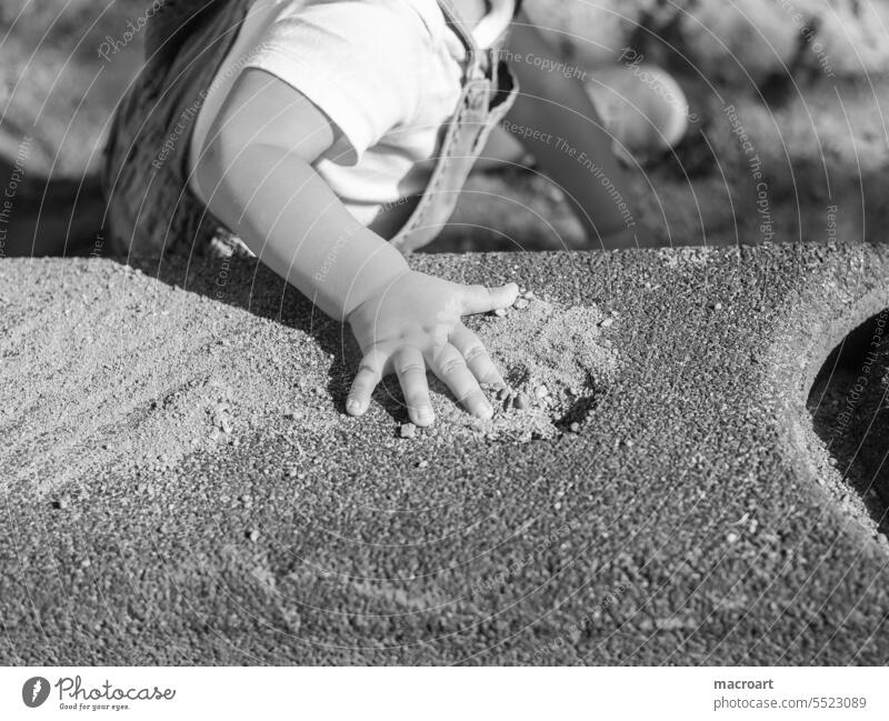 Kinderhand auf einem Spielplatz auf einem Stein in Nahaufnahme kind spielplatz schwarz-weiß finger kindheit erziehung kinder detail closeup Kleinkind Spielen