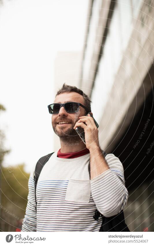Ein junger, reisender Mann mit Sonnenbrille, der mit einem Smartphone telefoniert, auf der Straße in einer spanischen Stadt. männlich Mobile Männer Erwachsener