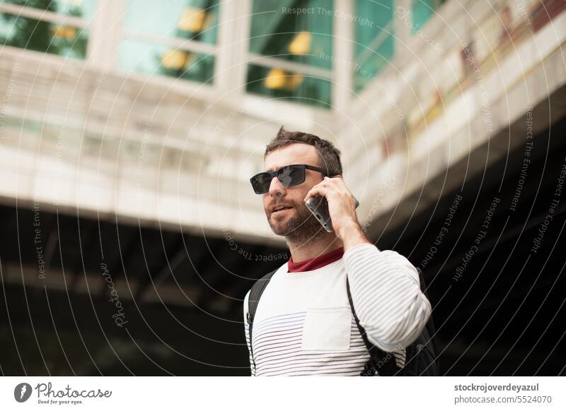 Ein junger, reisender Mann mit Sonnenbrille, der mit einem Smartphone telefoniert, auf der Straße in einer spanischen Stadt. Männer männlich Person urban