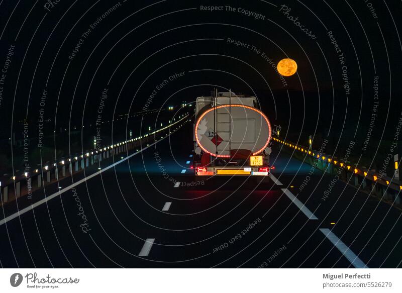 Tankwagen mit Gefahrenkennzeichen, der Kraftstoff transportiert und nachts mit dem Vollmond im Hintergrund fährt. Unretuschierte Fotografie, eine Einzelaufnahme.