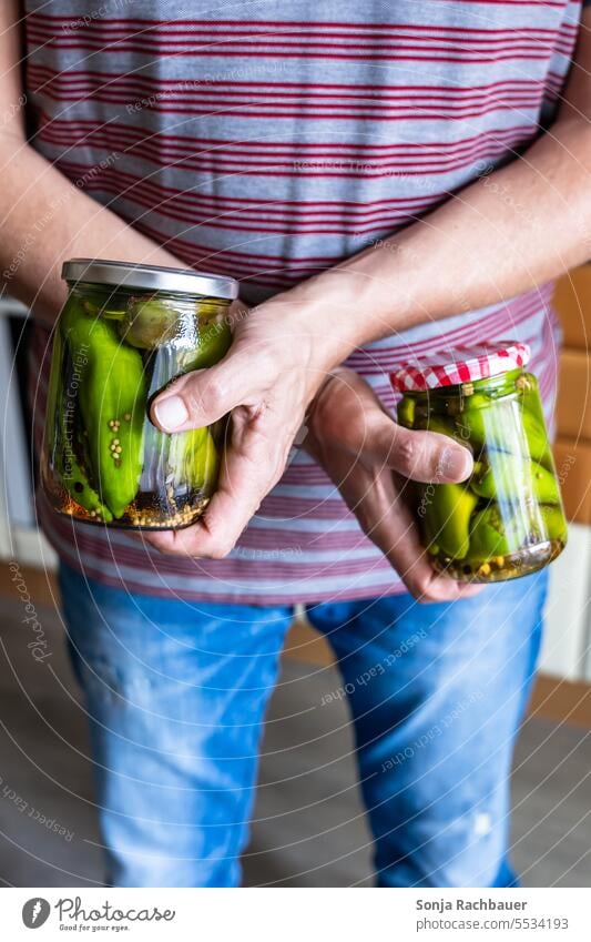 Ein Mann hält zwei Einmachgläser mit eingelegten Pfefferoni in den Händen Einmachglas halten Nahaufnahme 50 bis 60 Jahre Farbfoto Paprika konservieren