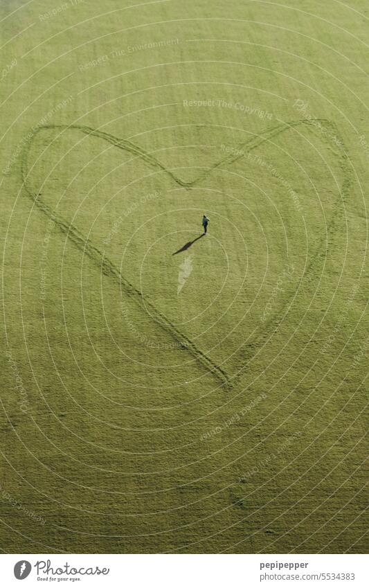 Herzlich willkommen – Luftaufnahme eines sehr großen Herzens auf einer Wiese gezeichnet. In der Mitte des Herzes steht eine Person, vermutlich die Person, die das Herz gezeichnet hat!