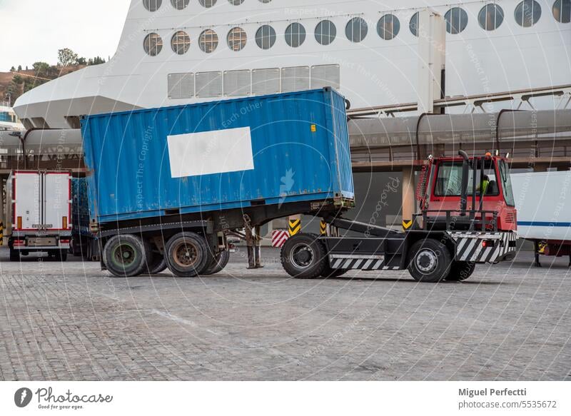 Spezielles Fahrzeug zum Entladen von Fähranhängern, ausgestattet mit einer hebbaren Sattelkupplung und automatischer Entriegelung, das einen Container transportiert.