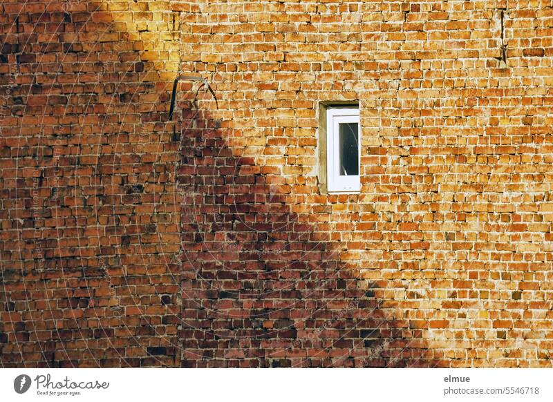 altes Gebäude aus unverputzten Ziegelsteinen mit einem kleinen Fenster und halb im Schatten Mauerziegel Ziegelsteinbau rot Altbau wohnen Ziegelsteinwand Teilung
