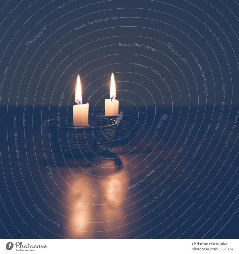 Zwei Kerzen auf dem Tisch bringen etwas Licht in den dunklen Raum Kerzenlicht Kerzenschein Kerzenflamme leuchten besinnlich Trauer brennende Kerze Glaube Gebet