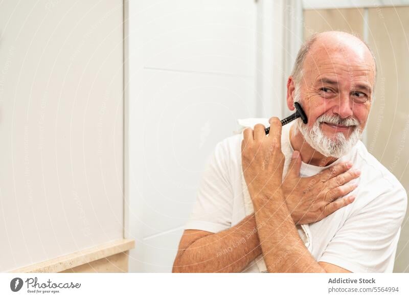 Erfreuter älterer Mann beim Rasieren im Badezimmer Rasierer Vollbart Pflege Rasierapparat Routine täglich Selbstversorgung männlich Senior Hygiene schäumen