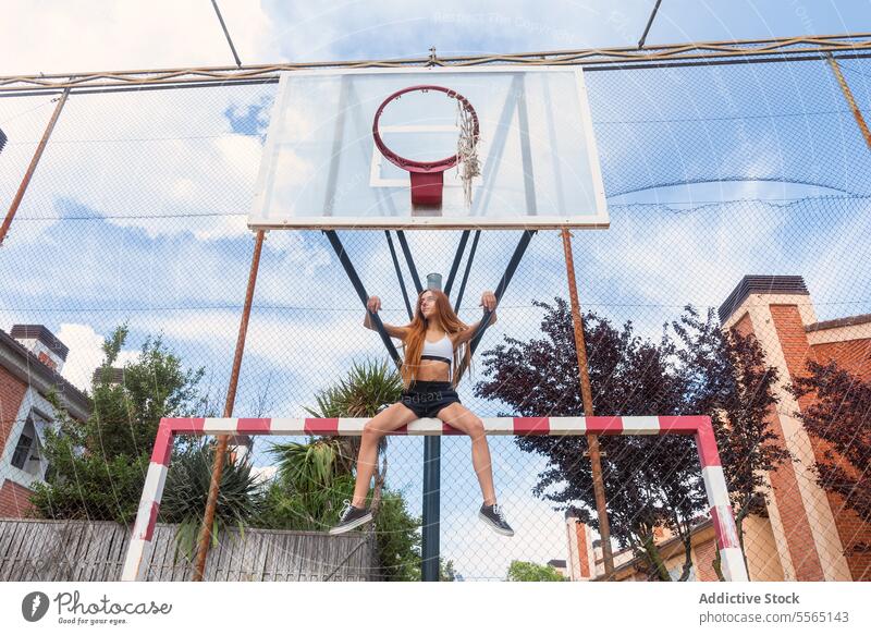 Rothaarige Frau hängt am Basketballring in der Stadt Rotschopf Ring erhängen Himmel im Freien Stärke Beweglichkeit Sport-BH schwarze Shorts sportlich Tatkraft