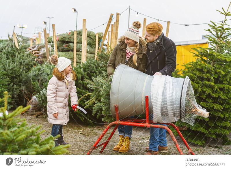 Eine Familie steht auf einem Straßenmarkt an einer Verpackungsmaschine für einen gefällten Weihnachtsbaum Teamwork kaufen Hilfsbereitschaft Kind Tochter