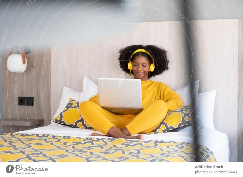 Schwarze Frau in digitaler Entspannung im modernen Schlafzimmer gelb Laptop Kopfhörer Bett sich[Akk] entspannen genießen Design Outfit Lächeln Kissen Muster