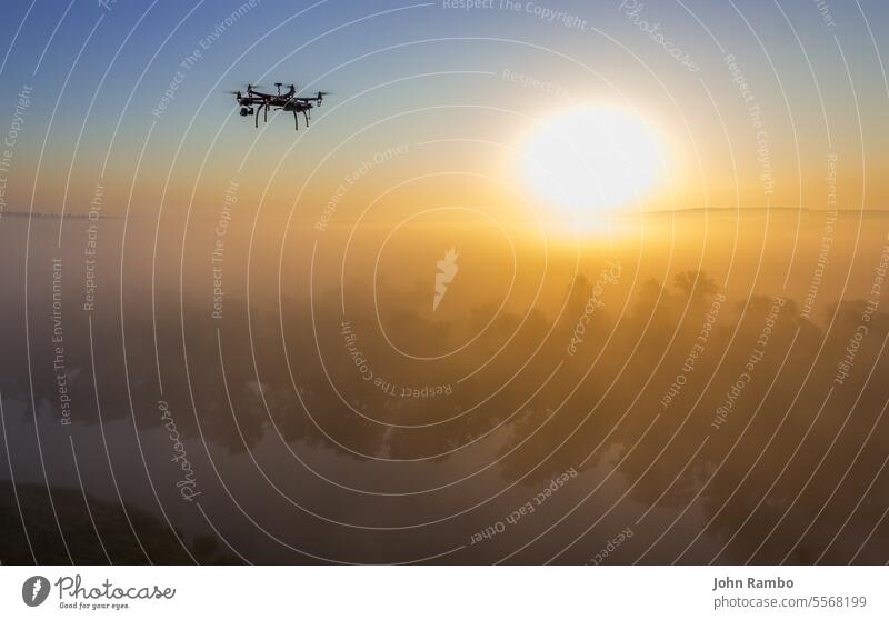 Hexacopter-Drohne über nebligem Sonnenaufgang am Fluss Hubschrauber modern Technik & Technologie Morgen schießen elektronisch Schweben spionieren Dröhnen