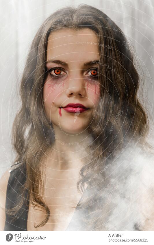 junge Frau im Nebel mit langen braunen Haaren, Halloween Makeup und gruseligen Pupillen Make-up Gesicht Farbe Kosmetik Schminke Auge Glamour Schönheit Model