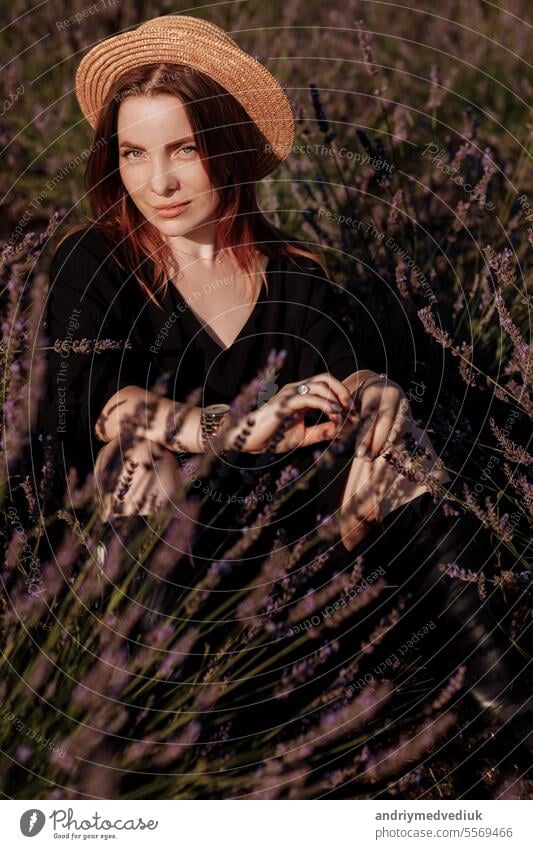 Junge romantische Frau in schwarzem Kleid und Strohhut sitzt in blühenden duftenden lila Lavendelfeld. Attraktives brünettes Mädchen genießt das Leben und träumt. Natürliche Schönheit Konzept
