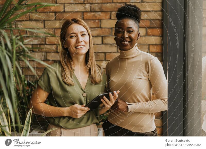 Zwei junge Geschäftsfrauen mit digitalem Tablet stehen an der Backsteinmauer in einem Büro im Industriestil Erwachsener Afrikanisch Amerikaner schwarz Business