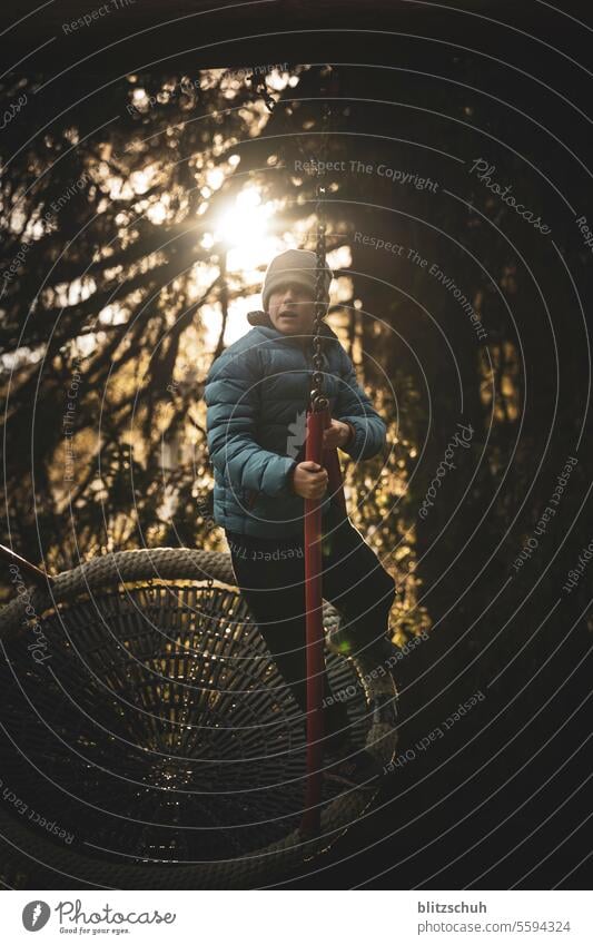 Ein Junge auf einer Netzschaukel im Gegenlicht authentisch Gefühle Leben im Freien Tourismus Berge Schweiz Lenzerheide Herbst Winter Fröhlichkeit Kind