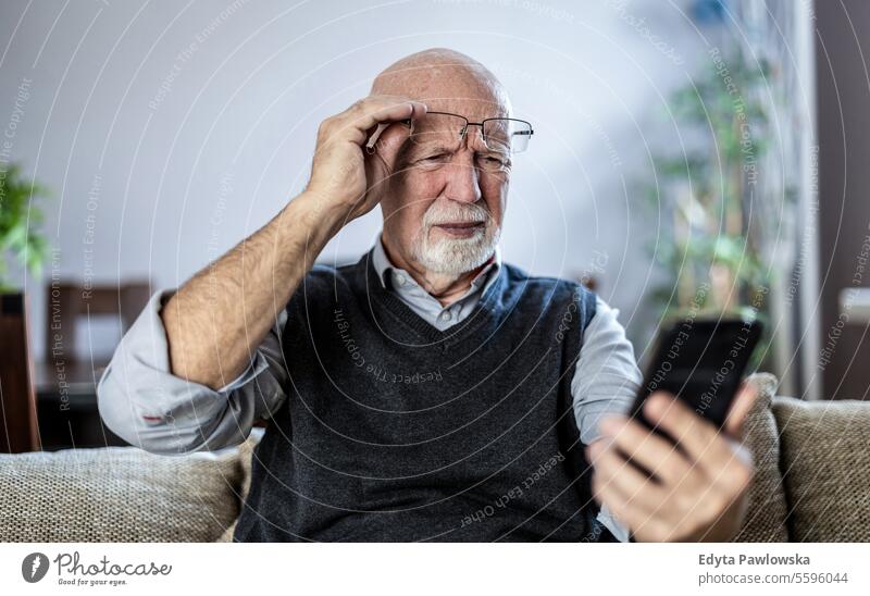 Älterer Mann starrt verwirrt auf sein Smartphone echte Menschen Senior älterer Erwachsener reif männlich Kaukasier heimwärts Haus alt Alterung häusliches Leben