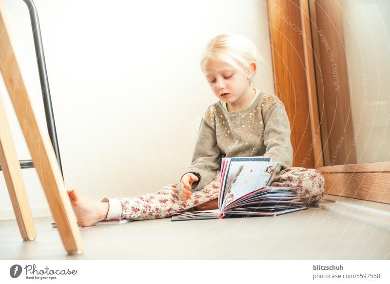 kleines Mädchen sitzt am Boden und schaut ein Kinderbuch an zuhause Lebensfreude Spielen Zufriedenheit stay at home Kindererziehung zuhause bleiben Fröhlichkeit