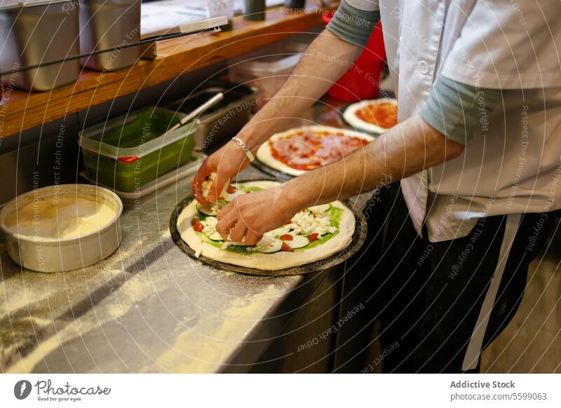 Pizzamann beim Belegen der Pizza mit Zutaten unkenntlich Mann Lebensmittel Pizzeria Käse Spinat Zucchini Saucen Restaurant Küche vorbereitend Italienisch
