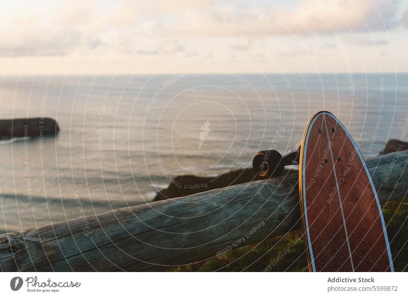 Surf-Skate lehnt an einem hölzernen Geländer gegen einen verschwommenen Strand Skateboard Longboard Brandung Schlittschuh Sport MEER Sommer im Freien