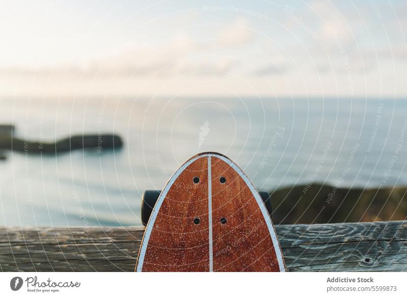 Surf-Skate lehnt an einem hölzernen Geländer gegen einen verschwommenen Strand Skateboard Longboard Brandung Schlittschuh Sport MEER Sommer im Freien