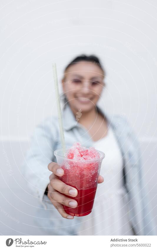 Eine junge hispanische Frau trinkt lächelnd einen mexikanischen Kirschslushy im Freien Sonnenbrille Schwarzes Haar blond Highlights Ohrringe Jeansstoff Jacke