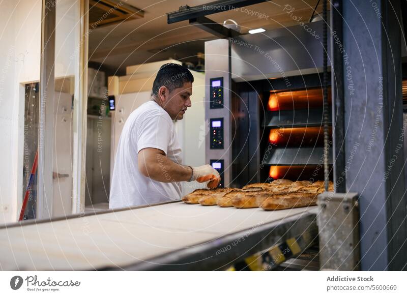 Latino-Bäcker nimmt Brot aus dem Ofen Mann lateinamerikanisch Förderband Gurt Gerät Bäckerei Kommissionierung Automatisierung industriell Tablett Lebensmittel