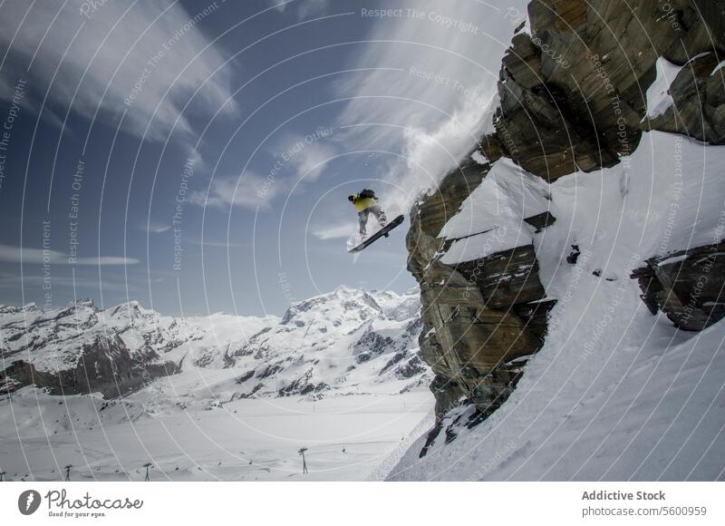 Anonymer Snowboarder, der an einem Wintertag bei bewölktem Himmel in den Schweizer Alpen vom Berg springt Person springen Berge u. Gebirge Felsen Snowboarding