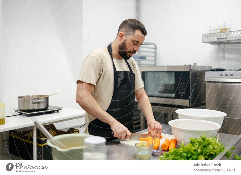 Junger Koch schneidet Karotten Küchenchef Essen zubereiten Lebensmittel professionell Restaurant Gemüse Messer Schneiden Mann jung Arbeit männlich Speise Person