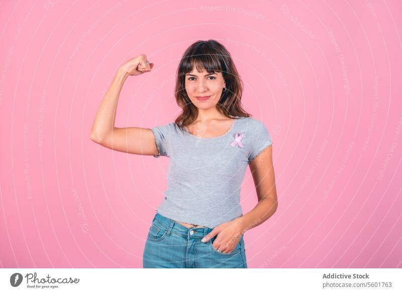 Eine Frau trägt ein rosa Brustkrebs-Band und zeigt ihre Armmuskeln. Sieg über Brustkrebs. Bewusstsein für Brustkrebs Brustkrebsmonat Prävention von Brustkrebs