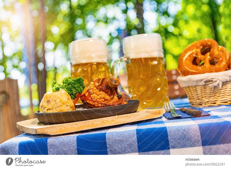 Schweinshaxe, traditionelle bayerische Küche mit gebratener Schweinshaxe mit Kartoffelknödel, Brezen und Bierkrug auf einem Tisch im Biergarten Brezeln