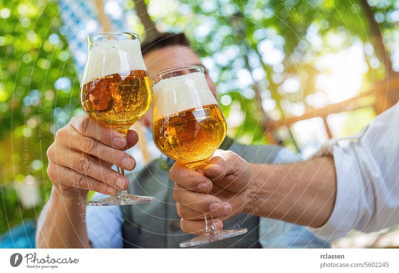 Bayerische Freunde, die in einem Biergarten oder auf einem Oktoberfest bei traditioneller bayerischer Küche mit Bierkrügen anstoßen Hand schäumen Großvater