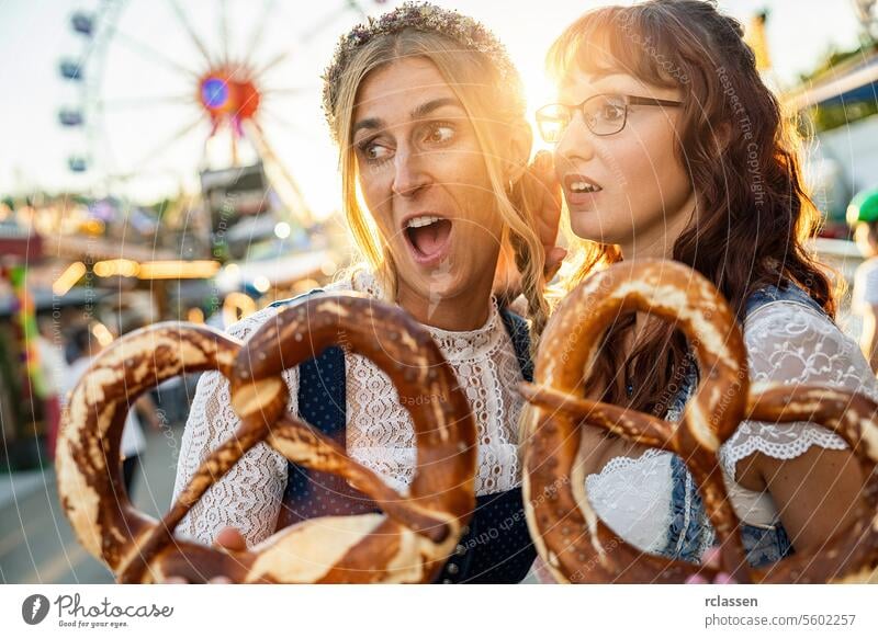 Zwei Freundinnen schauen staunend mit Brezel oder Brezen auf eine bayerische Messe oder Oktoberfest oder in Tracht oder Dirndl Frau Party brezen biergarten
