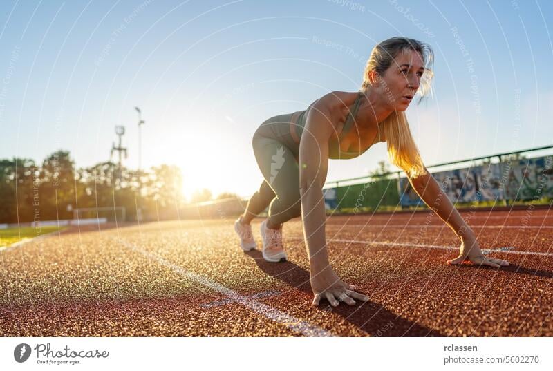 Weibliche Athletin in Startposition auf einem Leichtathletikfeld bei Sonnenuntergang Sportlerin Ausgangsposition Tatkraft Sportbekleidung Fitness Sprinter