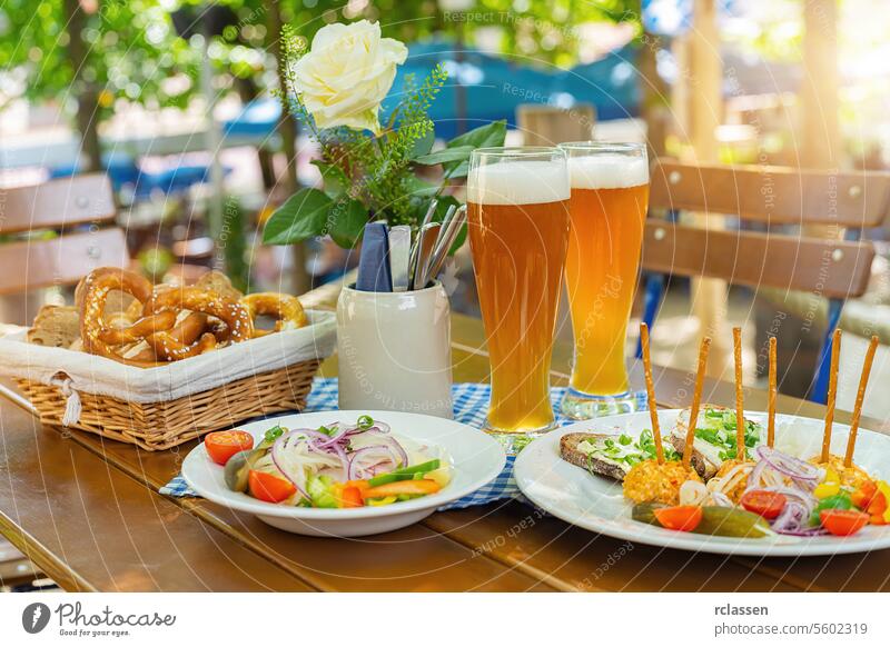 Traditionelles Biergarten-Essen mit obatzter Bierkrüge mit frischen Brezeln oder Brezen und Brot auf dem Oktoberfest, München, Deutschland jubelt Kellner